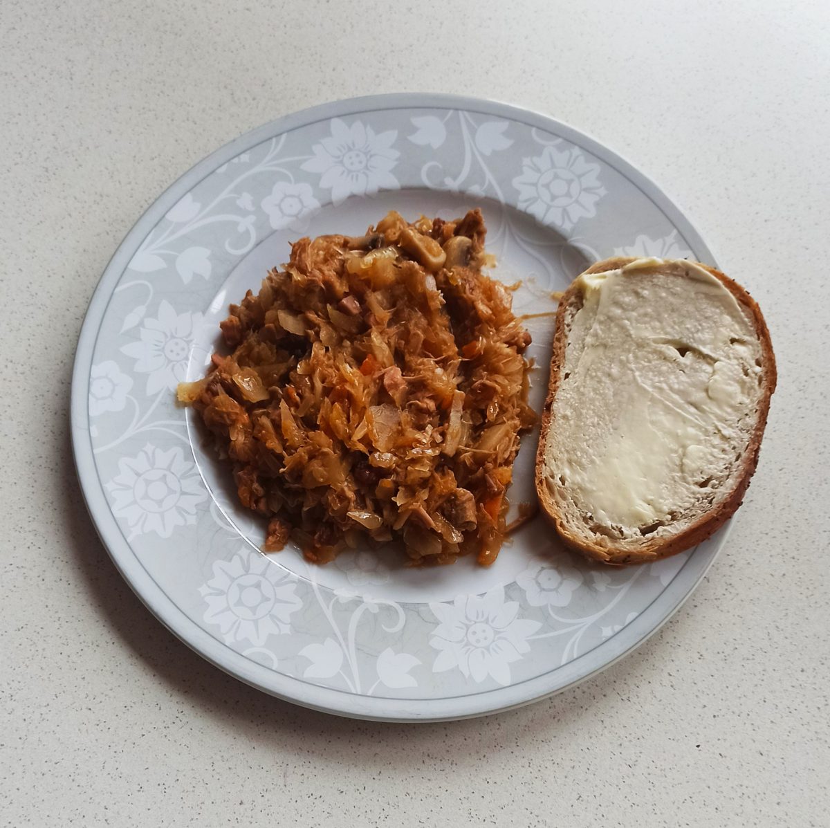 Domowy bigos na talerzu z kromką chleba z masłem