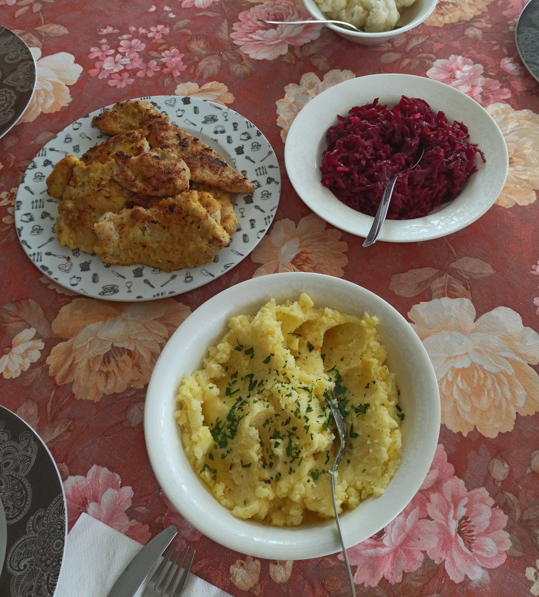 Domowy obiad: panierowane kotlety z indyka, ziemniaki puree i miska tartych buraczków na obrusie w kwiaty