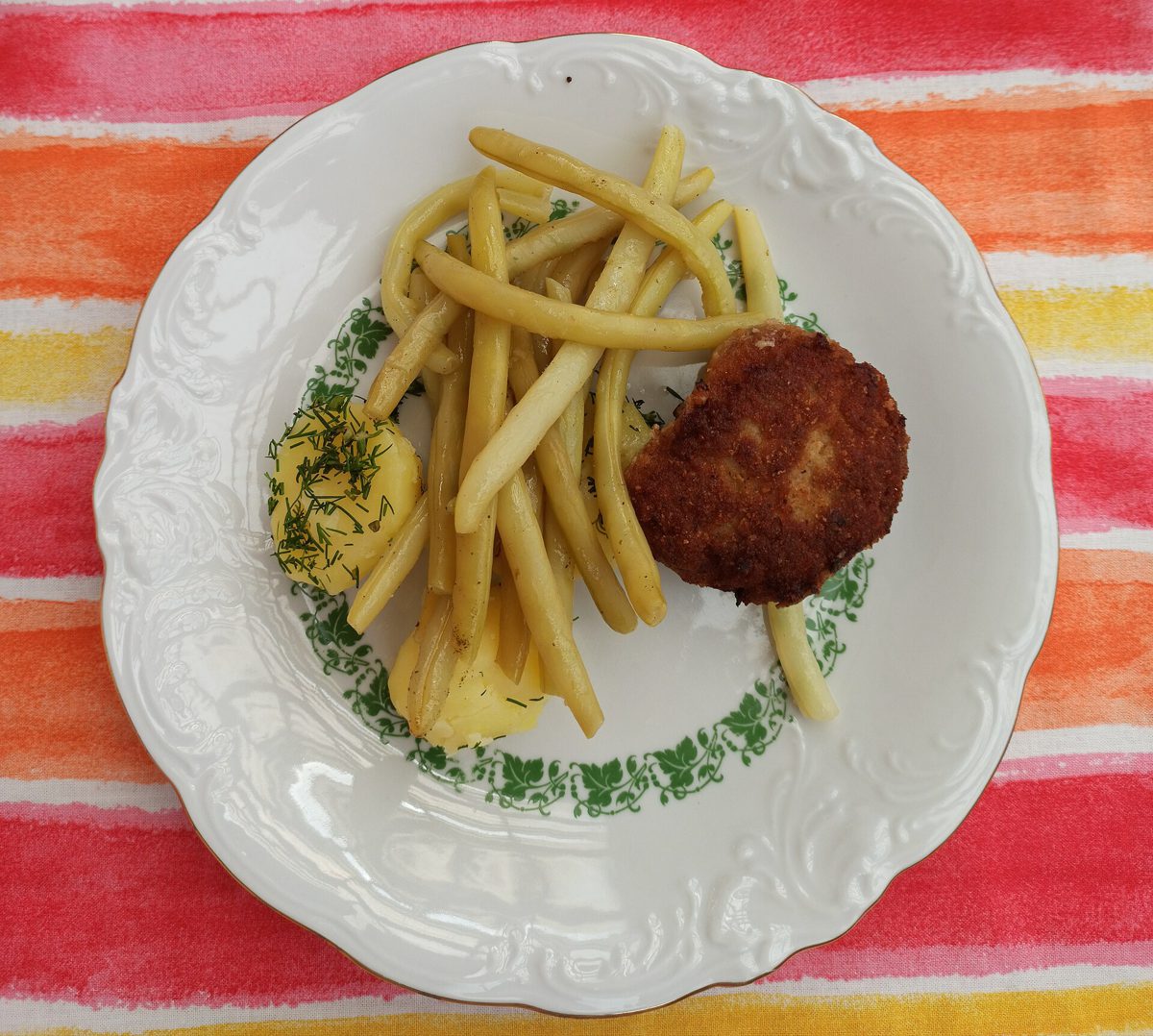 Kotlet mielony, ziemniaki z koperkiem i żółta fasolka szparagowa na białym talerzu