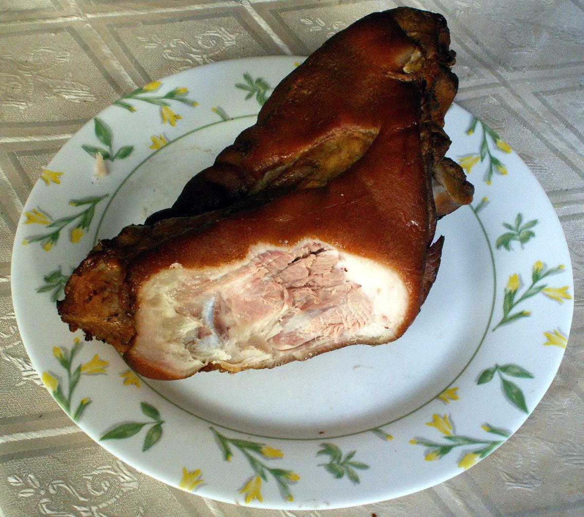 Pieczona golonka z ciemną, błyszczącą skórą, przekrojona, na talerzu w kwiaty