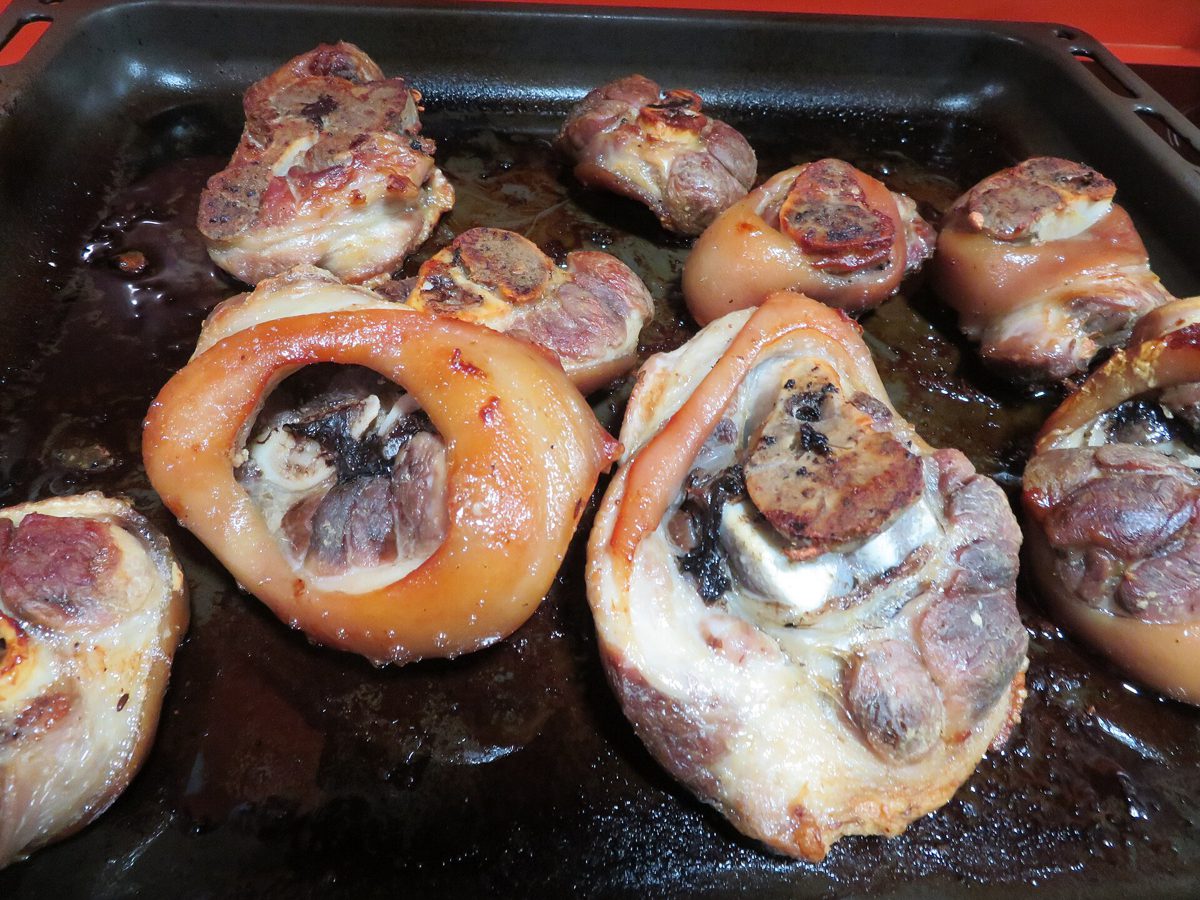 Pieczone golonki na ciemnej blasze, widać przekrój z kością