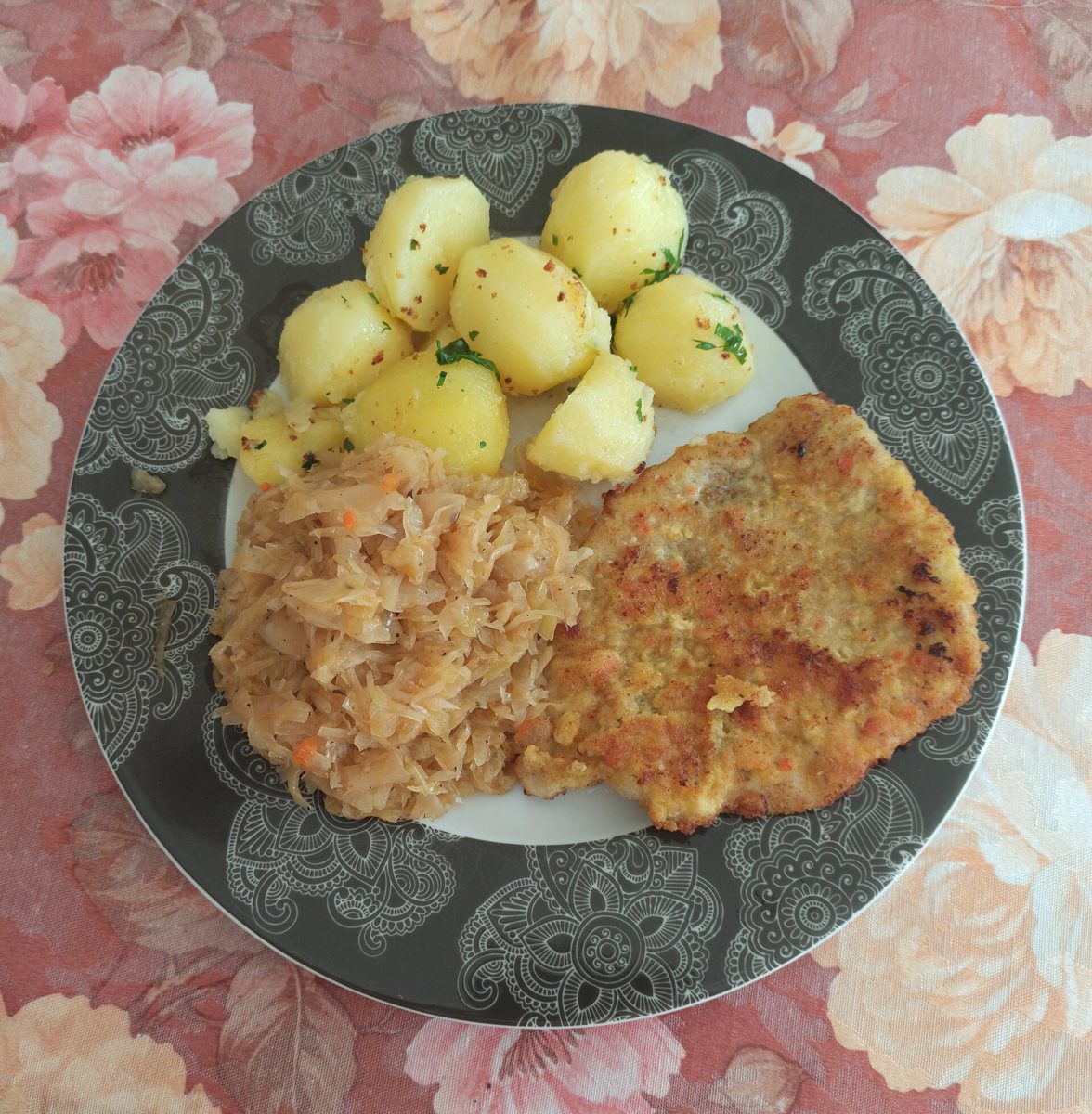 Kotlet schabowy, ziemniaki z koperkiem i duszona kapusta kiszona z marchewką na szarym talerzu