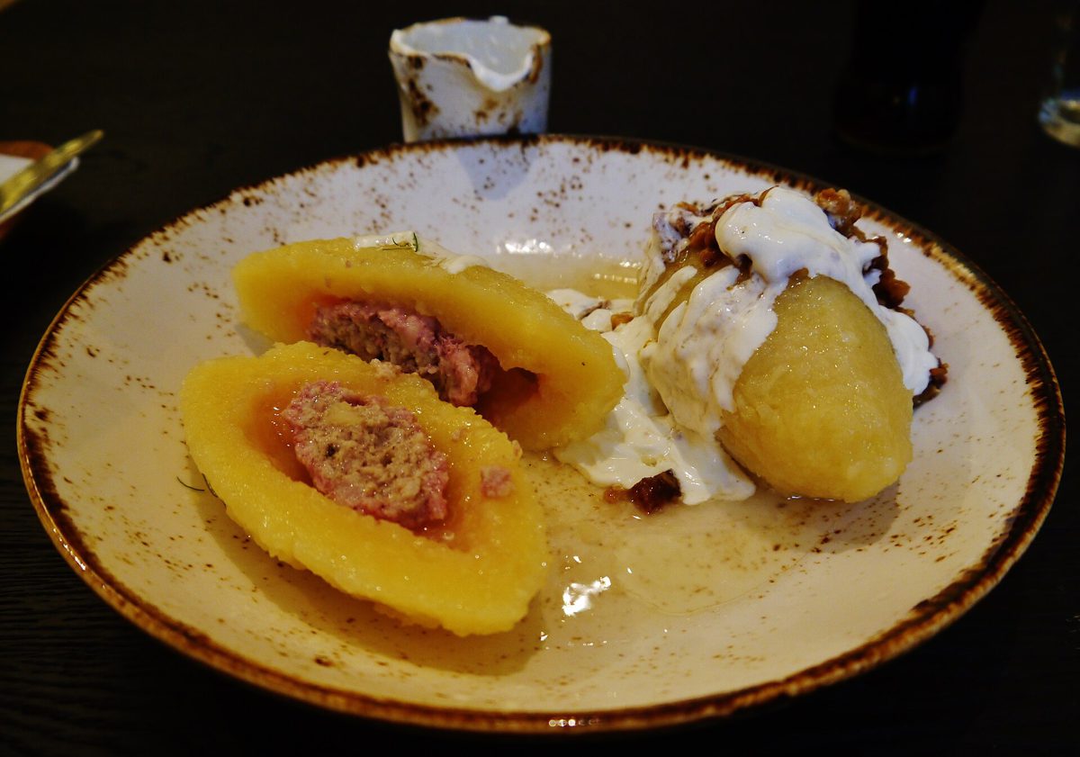 Cepeliny z mięsem i kwaśną śmietaną, jeden przekrojony na pół z widocznym mięsnym farszem, restauracja w Wilnie