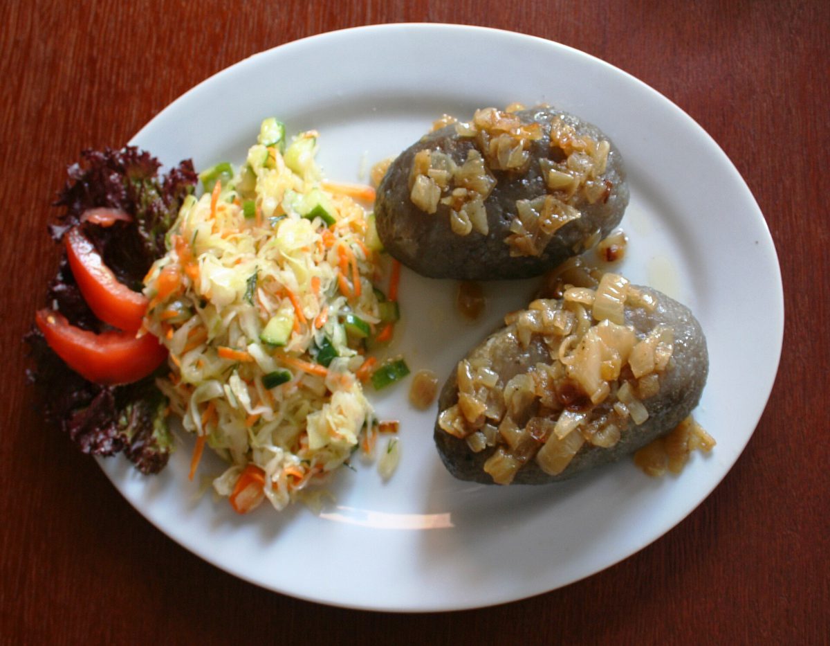 Dwa ciemnoszare kartacze z okrasą z cebuli i surówką z kapusty i marchewki, w restauracji w Goniądzu