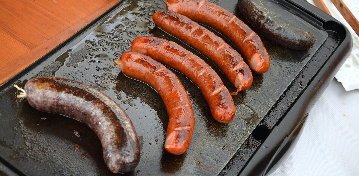 Dwie kaszanki w osłonce pieczone na płycie grilla elektrycznego obok kiełbas