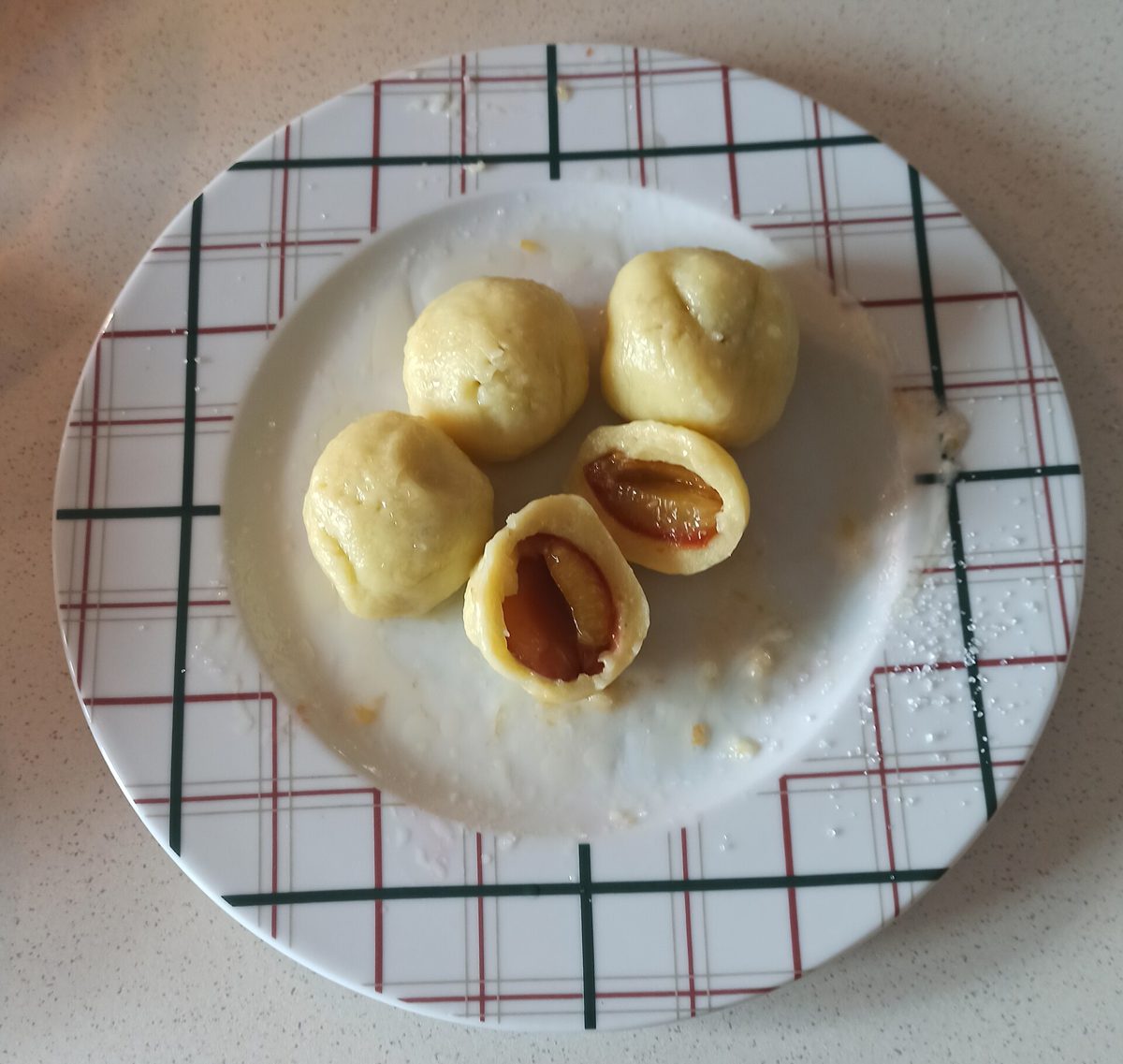Domowe knedle ze śliwkami na talerzu w kratkę, jeden przekrojony na pół