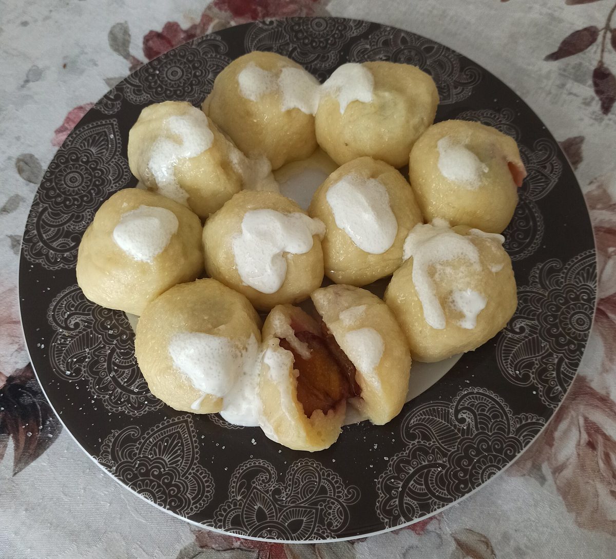 Knedle ze śliwkami polane śmietaną na ciemnym talerzu