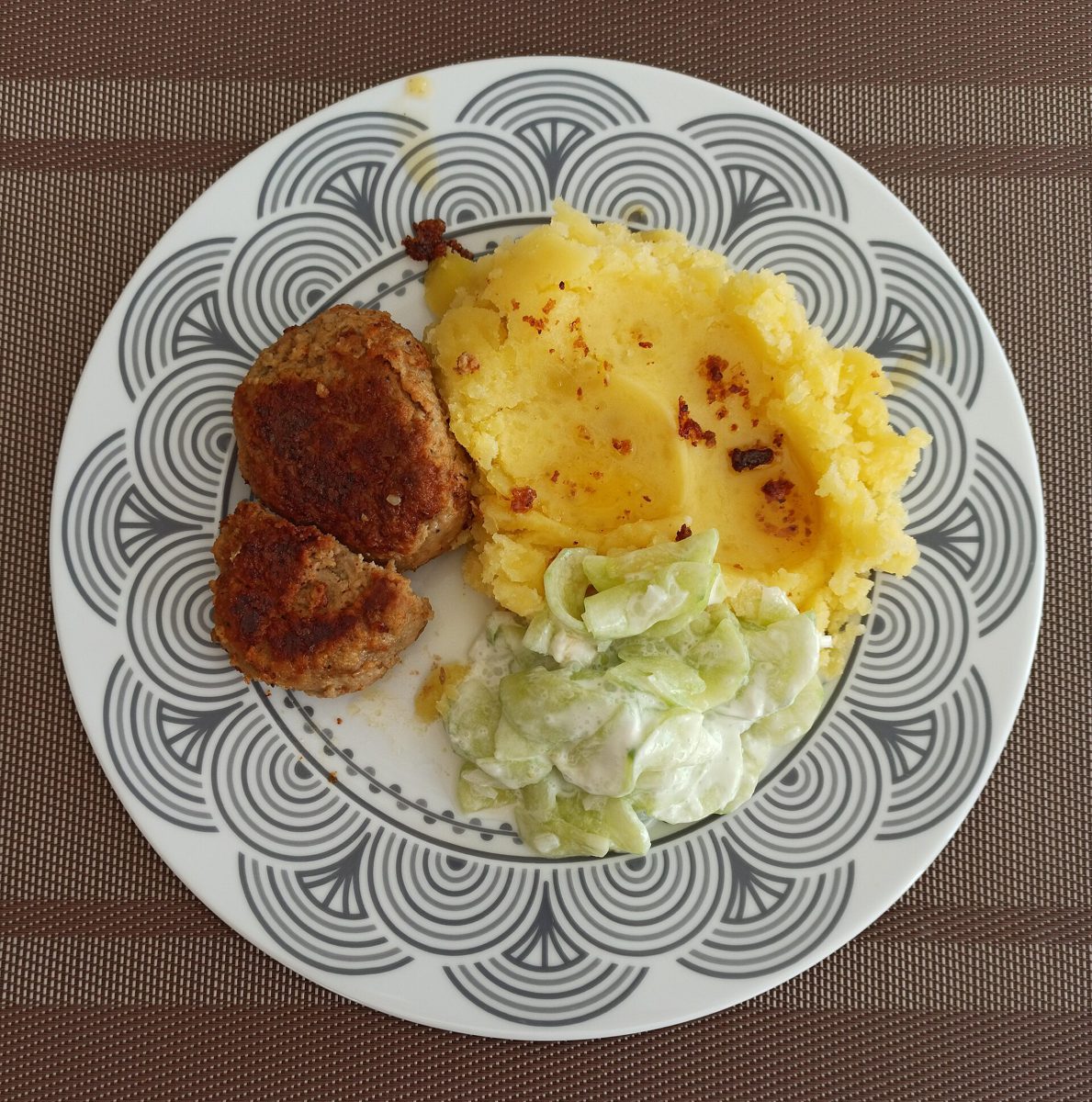 Dwa kotlety mielone z puree ziemniaczanym i mizerią na talerzu we wzory