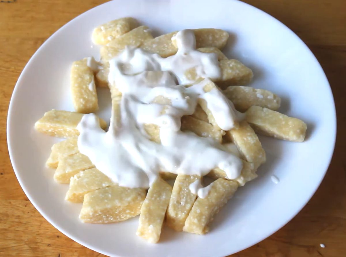 Pierogi leniwe polane jogurtem naturalnym na białym talerzu