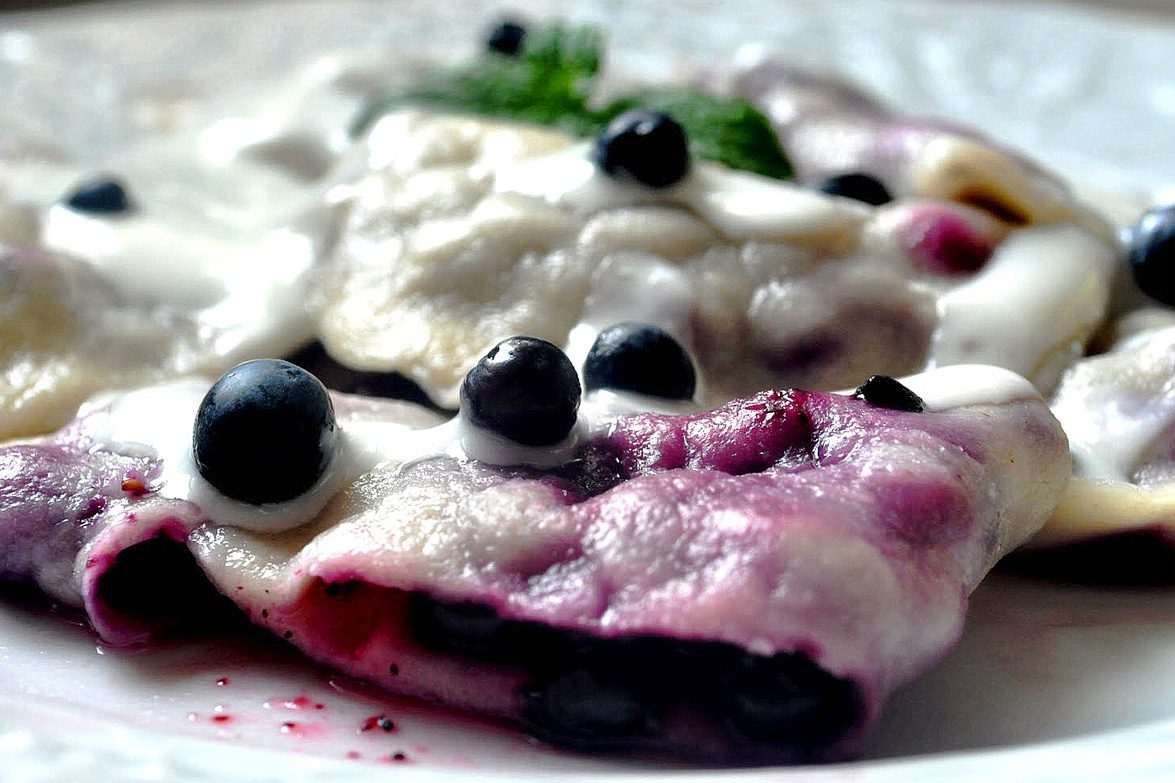 Pierogi z jagodami pod białą śmietaną, z fioletowym sokiem z owoców