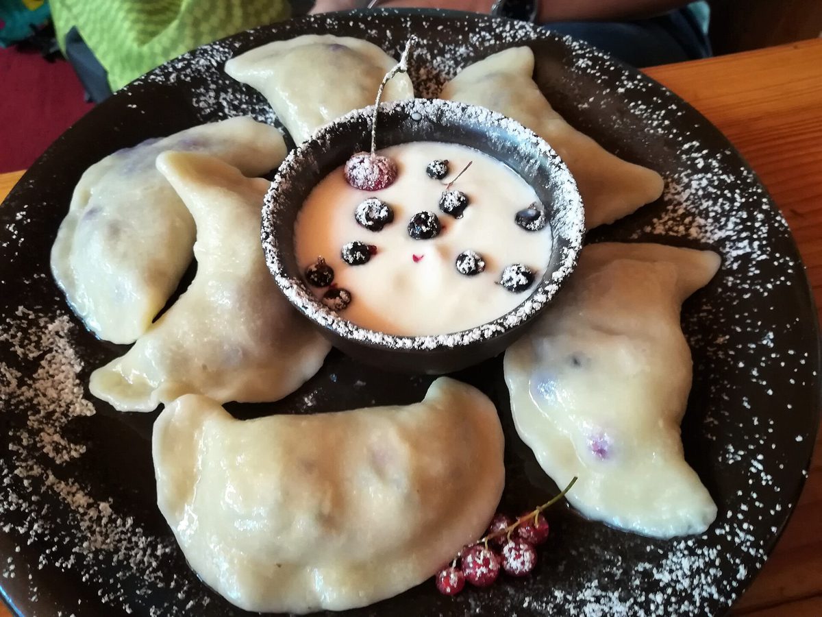Pierogi z jagodami ułożone wokół miseczki ze śmietaną, posypane cukrem pudrem