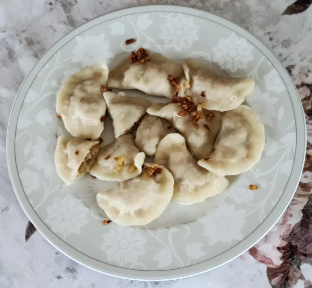 Pierogi z kapustą z przysmażoną cebulką na talerzu, jeden przełamany
