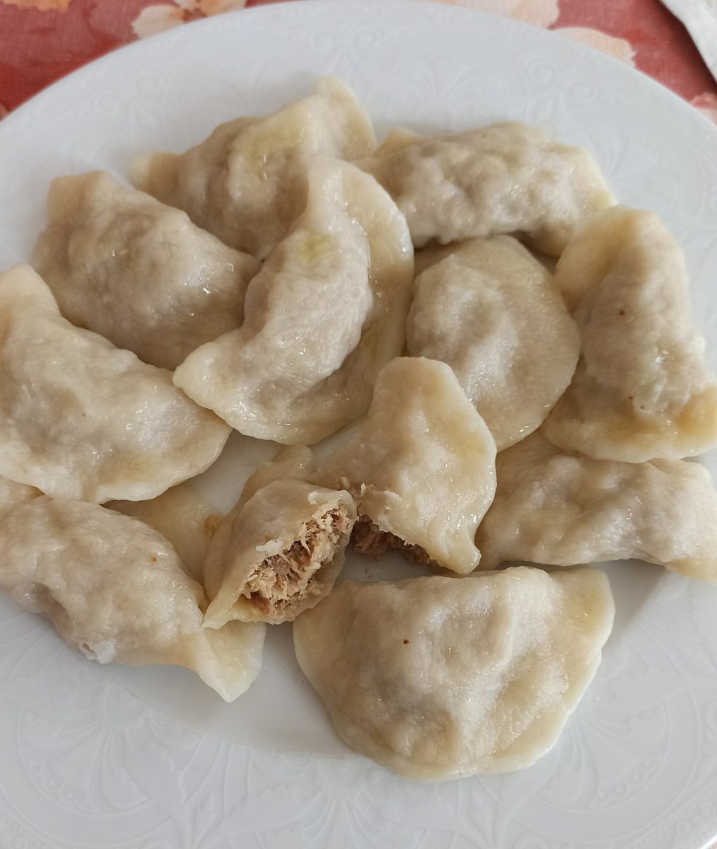 Ugotowane pierogi z mięsem, jeden przekrojony, z widocznym farszem z mielonego mięsa