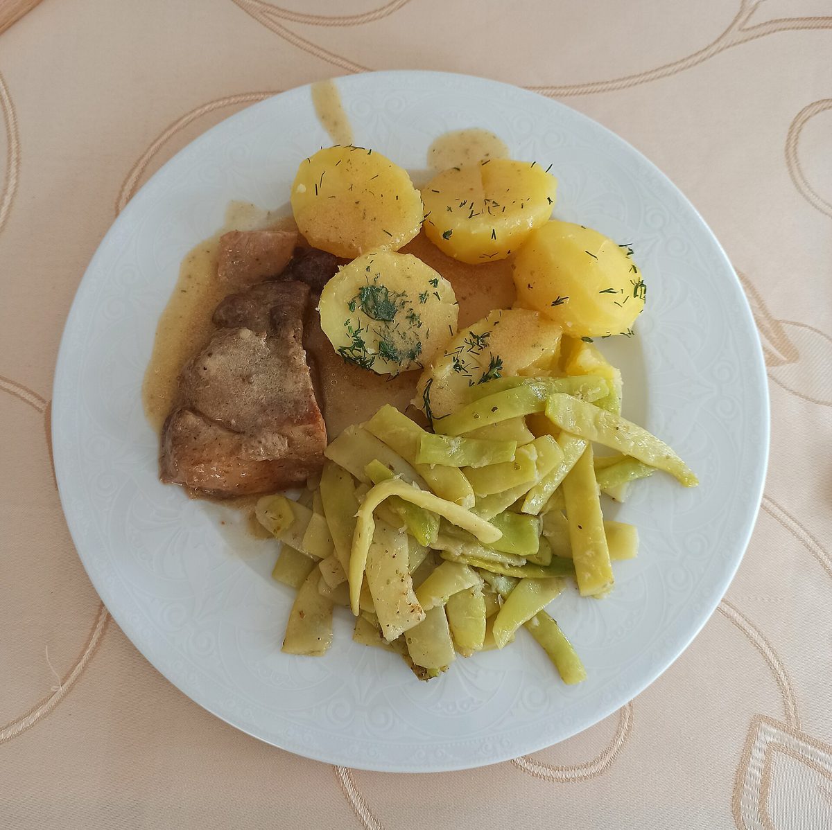 Pieczeń wieprzowa z sosem, ziemniakami z koperkiem i żółtą fasolką szparagową na talerzu