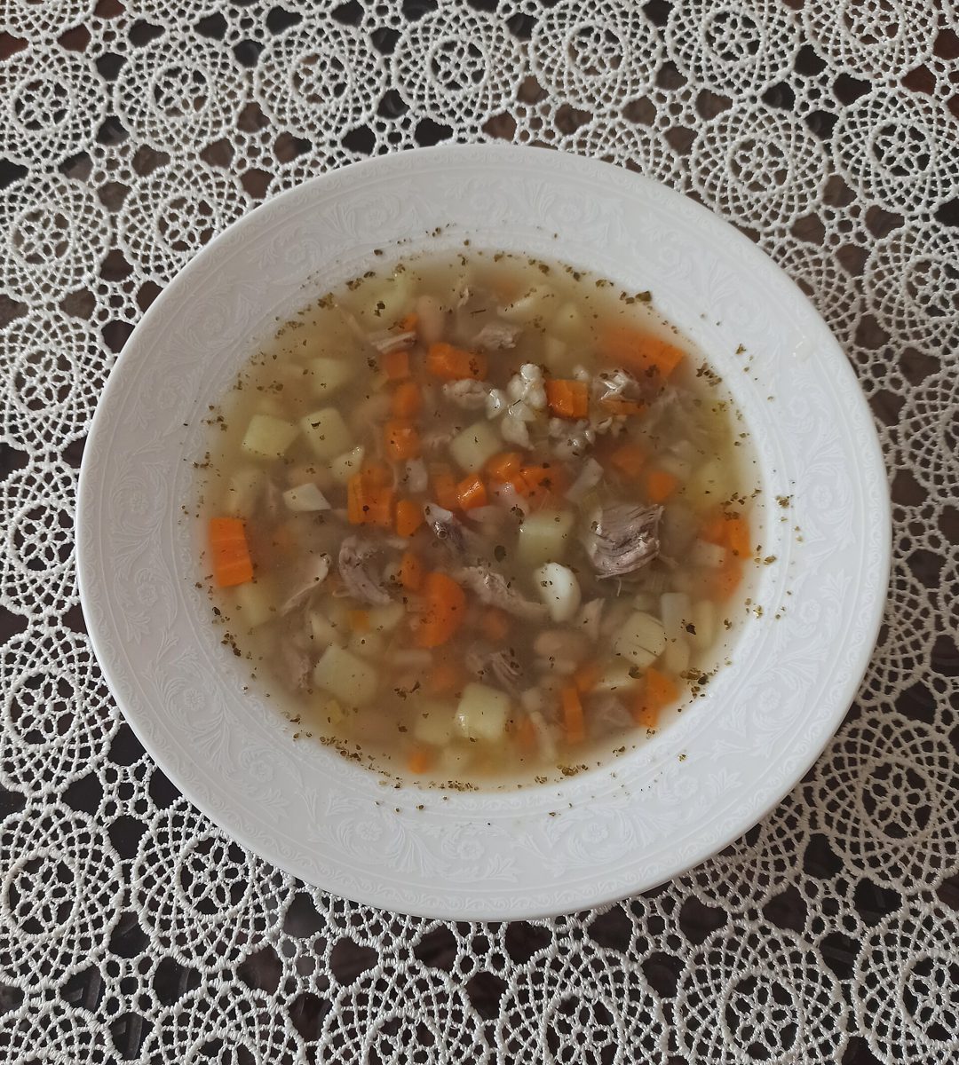 Zupa fasolowa z marchewką, ziemniakami i mięsem na talerzu, na koronkowym obrusie