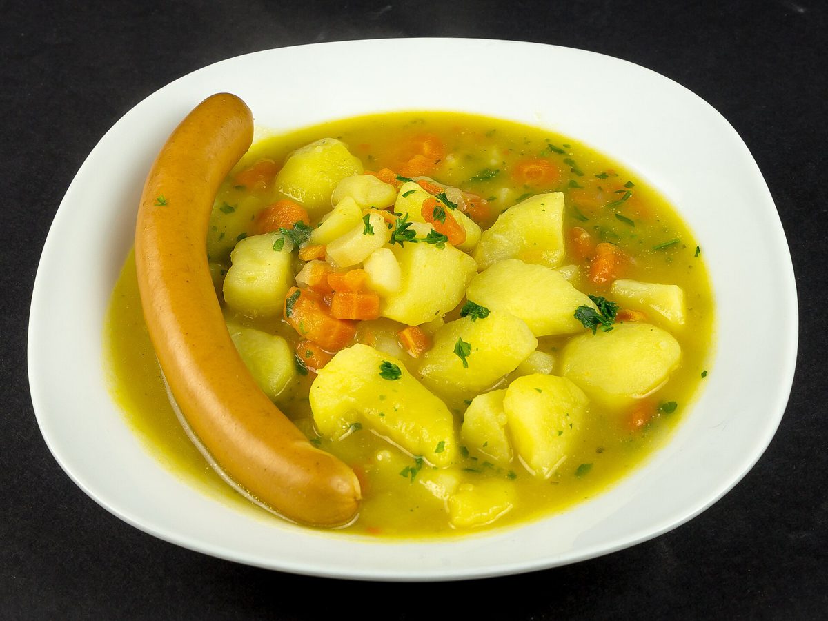 Gęsta niemiecka zupa ziemniaczana z marchewką, natką i parówką Bockwurst na białym talerzu